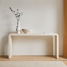 a white vase with flowers sitting on top of a wooden table next to a bowl