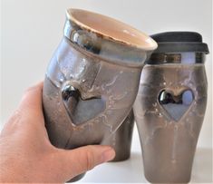 two handmade coffee mugs in the shape of hearts are being held by a person's hand