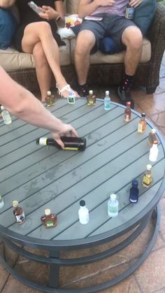 a group of people sitting around a coffee table with bottles on it and one person pointing at the bottle