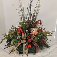 a christmas arrangement with pine cones, berries and a teddy bear sitting on top of it