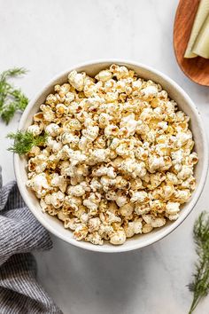 a white bowl filled with popcorn next to a wooden spoon and some parsley on the side