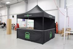 a black tent with green lettering on it in a warehouse area next to boxes and other items