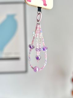 a cell phone hanging from a hook with beads and charms on it's side