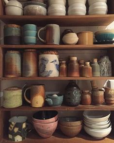 a shelf filled with lots of different kinds of dishes and cups on top of wooden shelves