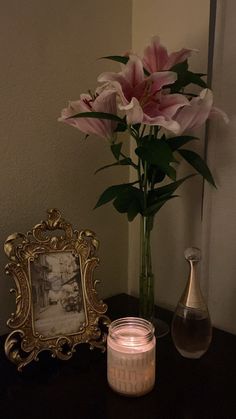 a vase with pink flowers and a candle on a table next to a framed photograph