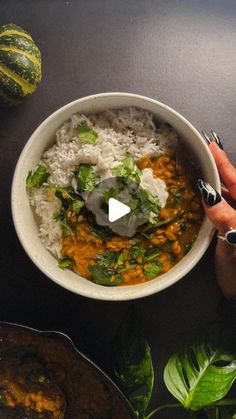 a person holding a bowl of food with white rice and vegetables in it on a table