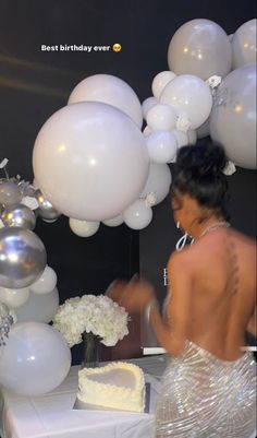 a woman cutting into a white cake on top of a table next to balloons and flowers