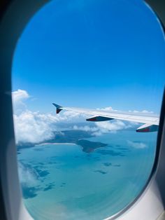 an airplane window looking out at the ocean and land below it, with clouds in the sky