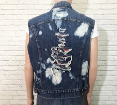 "1980's Levis denim vest. Cut off frayed sleeves with holes and bleach splashes throughout. Non-bulky fit. Dual front chest patch pockets with buttoned flaps. Perfect for adding your own patches + pins to. ✂ Measurements ✂ Labelled size: 45 Fits like: Mens 45 / Medium To Large depending on desired fit // Ladies Large ✂ Measurements: ( taken laying flat and buttoned ) Shoulders: 19.5\" Length: 24.25\" Chest: 22.5\" Waist: 21.25\" Waistband: 20.5\" Label + Fabric Levis Made in U.S.A 100% Cotton Co Sleeveless Grunge Vest For Spring, Cotton Grunge Denim Vest For Spring, Fitted Grunge Vest For Festivals, Edgy Sleeveless Denim Vest For Spring, Grunge Sleeveless Vest For Spring, Distressed Medium Wash Denim Vest For Summer, Distressed Medium Wash Vest For Spring, Medium Wash Distressed Denim Vest For Summer, Edgy Cotton Denim Vest For Summer