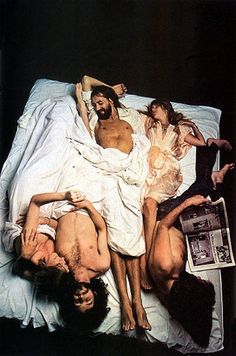 several people laying on a bed with one person in the middle and two others lying down