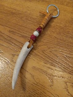 a knife shaped like a keychain on top of a wooden table with a red bead around it