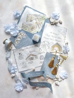 an assortment of paper and crafting items on a white surface with blue flowers around it