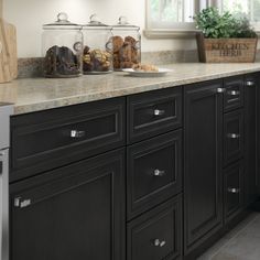 a kitchen with black cabinets and marble counter tops, along with glass jars filled with pastries