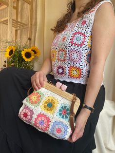 a woman sitting on a chair holding a purse with crocheted flowers in it