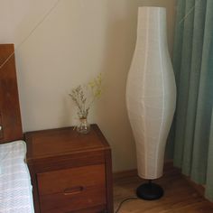 a white vase sitting on top of a wooden table next to a bed and nightstand