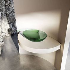 a green glass bowl sitting on top of a white table next to a rock wall