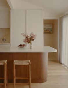 two stools are in front of the kitchen island with flowers on it and an open window