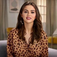 a woman sitting on top of a couch in front of a window wearing large hoop earrings