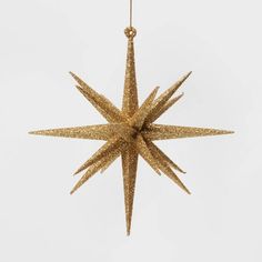 a gold glittered star ornament hanging from a string on a white background