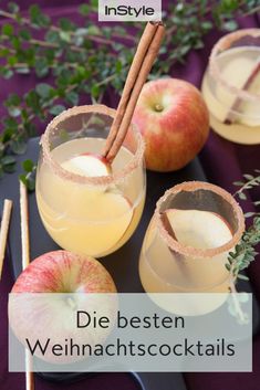 two glasses filled with apple cider on top of a black tray next to apples and cinnamon sticks