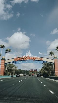 the entrance to disney world with cars driving under it and palm trees on either side