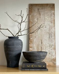 two black vases sitting on top of a wooden table next to a book and tree branch