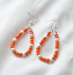 These handmade orange and white beaded earrings are the perfect addition to any outfit. They are lightweight, comfortable, and made of hypoallergenic materials.  2.5 inches in length. You have the option of gold- or silver-colored ear hooks. Care Instructions: - Keep away from moisture - Remove when sleeping - Remove before entering water - Store in cool dry area - Gently wipe with soft cloth to clean These unique handmade earrings would make the perfect birthday gift, anniversary gift, bridesmaid gift, Christmas gift, Valentines day gift, mothers day gift, teacher gift, gift for her, and so much more!  Thank you so much for checking out my shop! Don't hesitate to message me with any questions!  - Tennessee Earrings, TN Jewelry, TN Vols Earrings, Tennessee State Colors, Tennessee Vols Earr White Beaded Teardrop Earrings, White Teardrop Beaded Earrings For Beach, White Teardrop Jewelry With Tiny Beads, Orange Teardrop Beaded Earrings As Gift, White Teardrop Beaded Earrings, White Teardrop Beaded Earrings For Pierced Ears, Orange Teardrop Beaded Earrings For Gift, Orange Teardrop Beaded Earrings With Ear Wire, Orange Teardrop Beaded Earrings With Dangling Beads