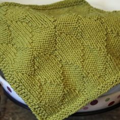 a green knitted blanket sitting on top of a bowl