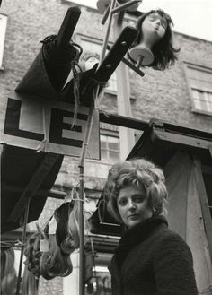 black and white photograph of two women standing in front of a street sign that has hair clips hanging from it