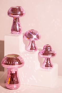 three shiny pink mushroom shaped objects sitting on top of a white blocky surface with light shining through them