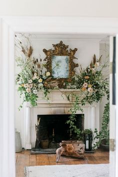 the fireplace is decorated with flowers and greenery in front of an ornate framed mirror