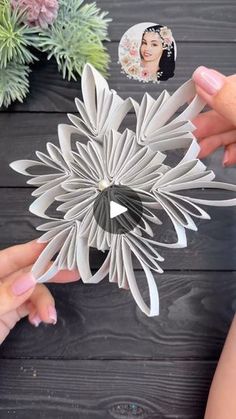 two hands are holding an origami flower on a wooden table with succulents