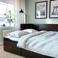 a bed with white sheets and two pictures on the wall above it, in front of a window