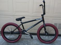 a black and red bmx bike parked in front of a garage with two doors