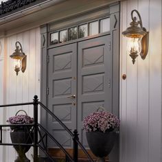 two lamps on the side of a building with flowers in front of it and another light above them