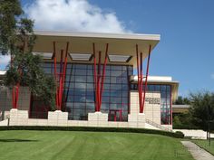 a large building with many windows and red poles on the outside, along with green grass