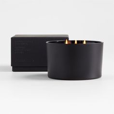 a black candle holder with three lit candles in it next to a box that says,