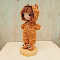 a crocheted teddy bear is standing on a wooden base and wearing a hoodie