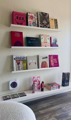 a white shelf with books on it and some pictures hanging from the wall behind it