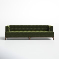 a green velvet couch with wooden legs on a white background in front of a wall