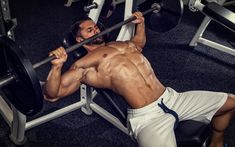 a shirtless man lifting a barbell in a gym