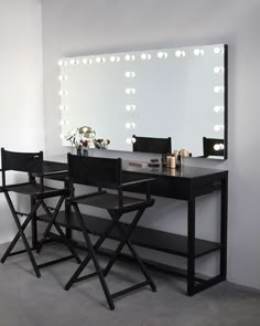 a vanity table with two chairs and a large mirror on the wall behind it that is lit up