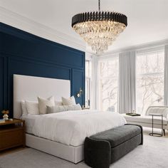 a bedroom with blue walls, white bedding and a chandelier hanging from the ceiling