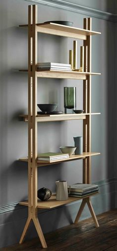 a wooden shelf with many books on top of it in front of a gray wall