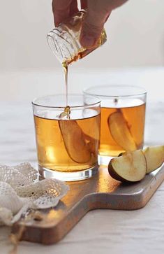 two glasses of honey bourbon apple cider cocktail are sitting on a wooden cutting board