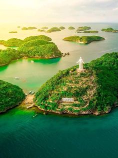 an island in the middle of water surrounded by green land and small islands with trees on each side