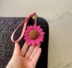 a hand holding a crocheted key chain with a pink flower attached to it