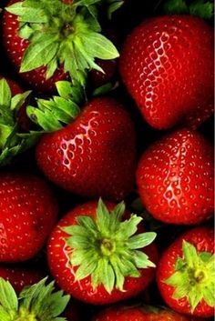 a pile of red strawberries with green leaves