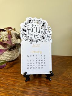 a desk calendar sitting on top of a wooden table next to a potted plant