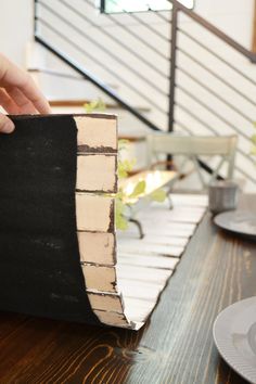 a person is holding up a piece of paper on top of a wooden table next to a cup and saucer